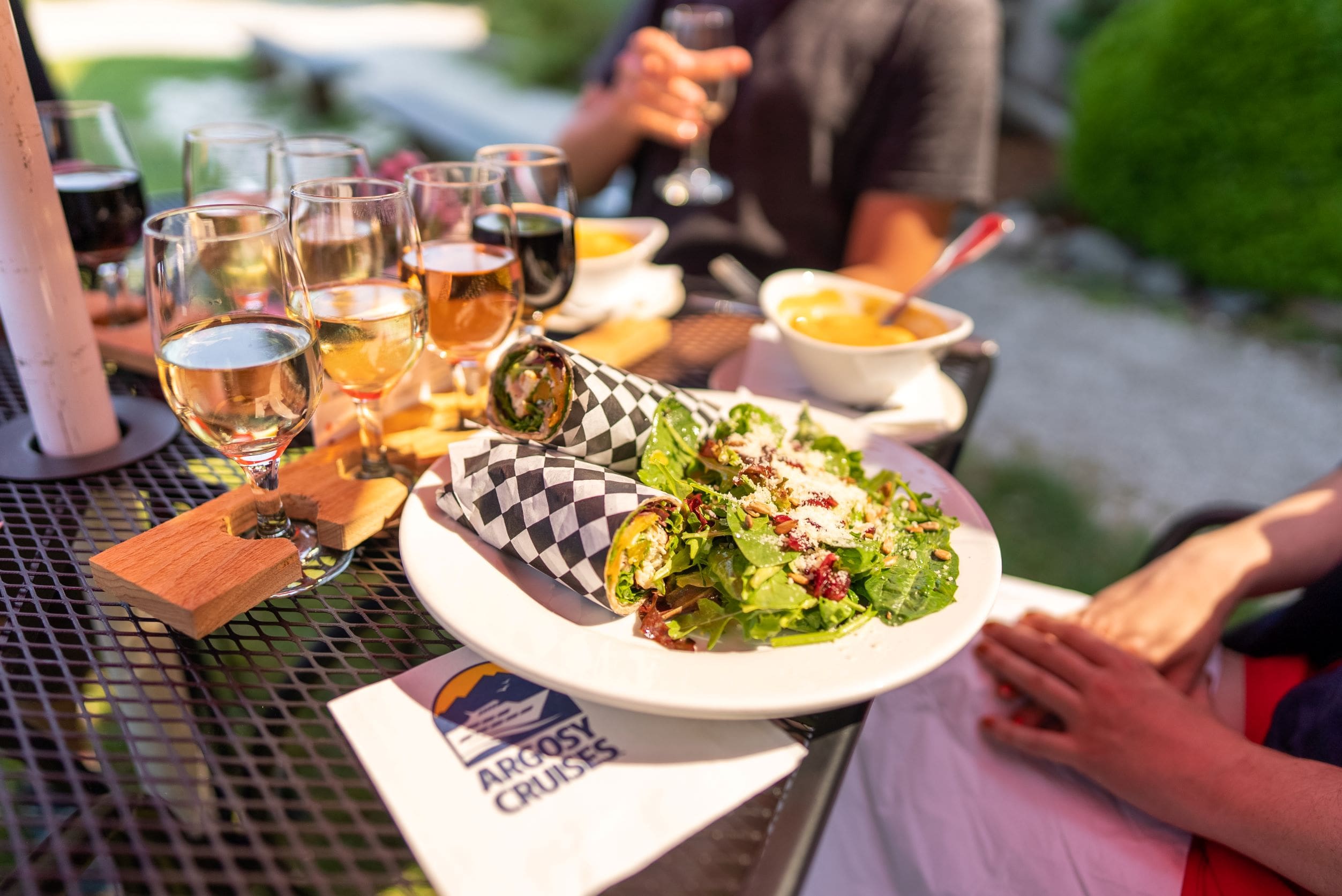 Salad and wrap on plate with wine glasses and man's hand in background