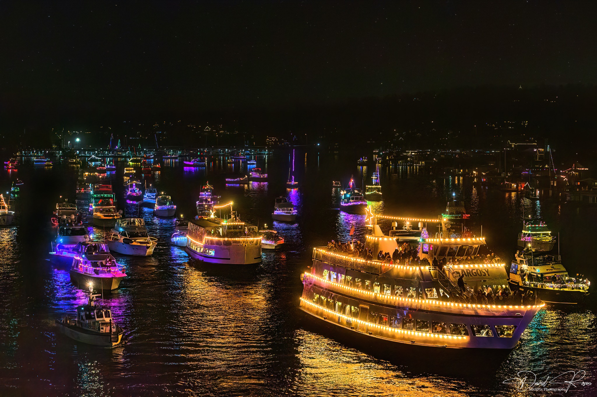 Christmas Ship Festival: Dozens of boats covered in dazzling Christmas lights cruise on dark water at night, part of a festive holiday ship parade.