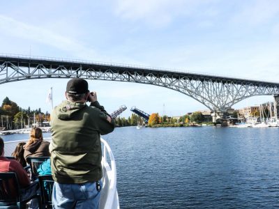From a boat, a photographer captures a large steel bridge, and an open drawbridge with a small boat passing through a channel.