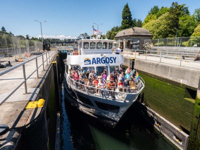 Locks Cruise: A large ARGOSY boat, crowded with people, travels through a narrow canal lock with green-tinged concrete walls.
