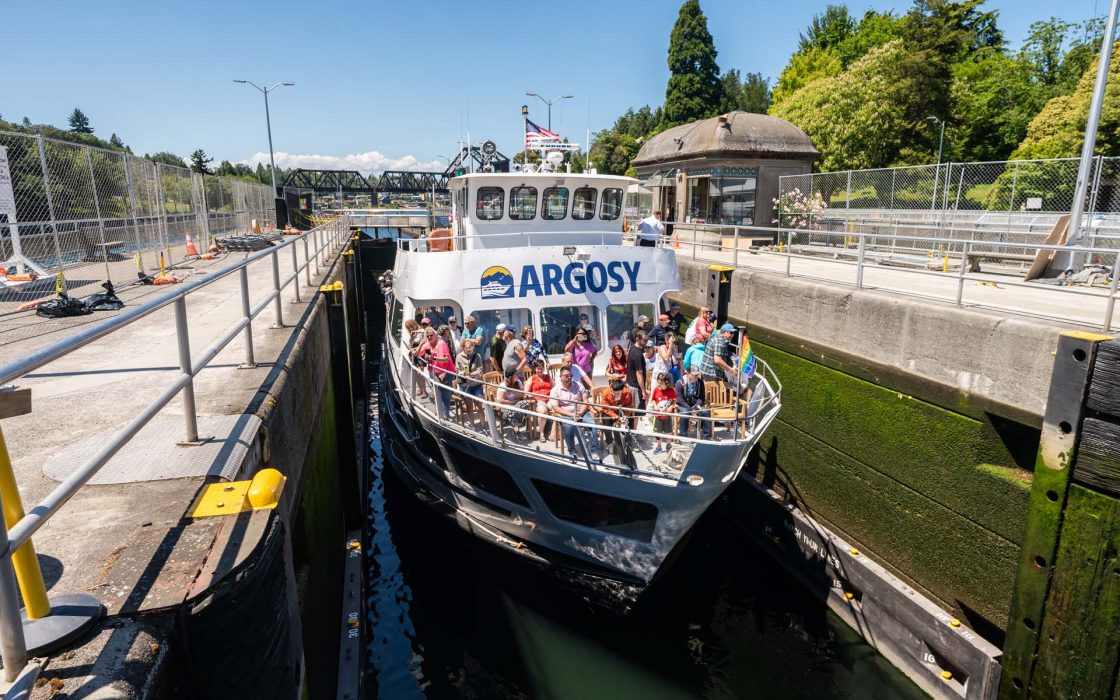 Locks Cruise: A large ARGOSY boat, crowded with people, travels through a narrow canal lock with green-tinged concrete walls.
