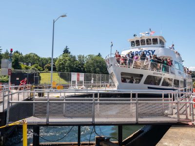 A busy passenger ferry, Goodtime III, is at a metal dock. People watch from the deck, with green hills and a bright sky.