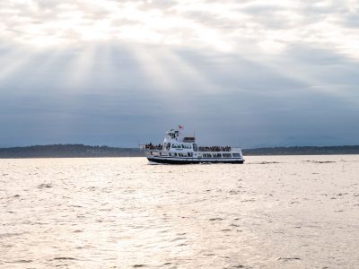 People enjoy a scenic cruise on a white Argosy ferry across reflective water, illuminated by sunbeams peeking through cloudy skies.
